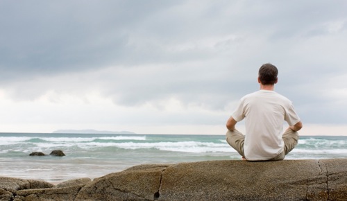 Man meditating on a rock at the sea