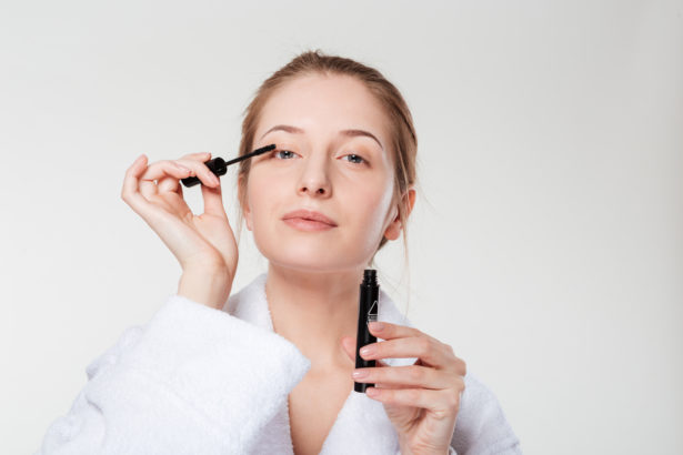 Woman applying mascara on eyelashes isolated on a white background