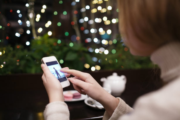 Woman in cafe drinking tea and looking through the photos in her smartphone