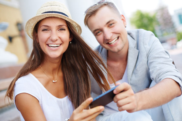 Happy dates with cellphone looking at camera outside