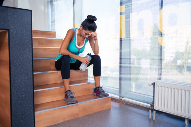 Tired woman sitting on the stairs with bottle of water in gym