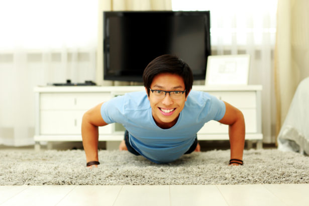 Portrait of a smiling young man doing push ups in the living room at home