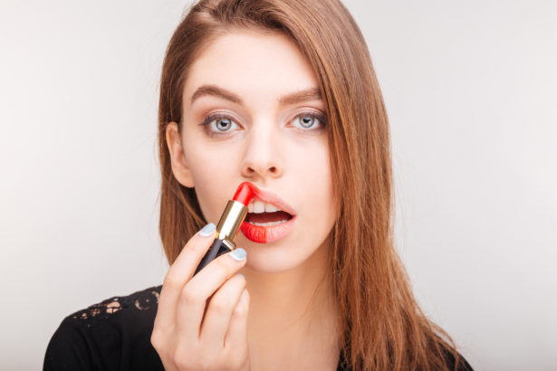 Beauty portrait of pretty woman doing makeup with red lipstick