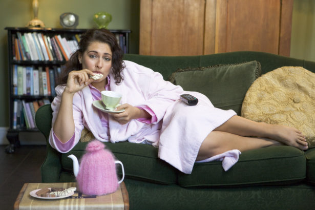 A young woman lying on her couch drinking tea