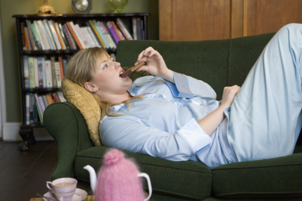 A young woman lying on her couch eating chocolate