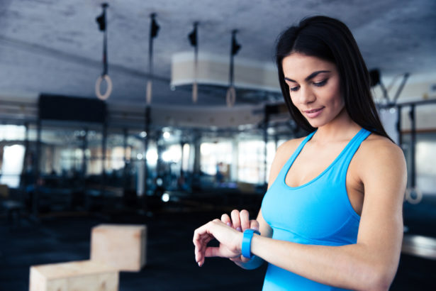 Happy young woman using activity tracker in fitness gym