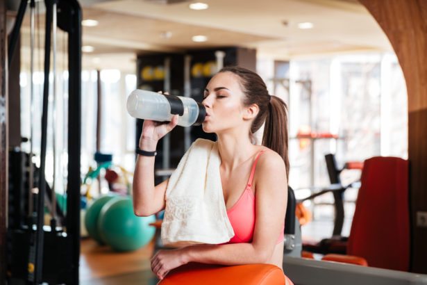 Woman athlete drinking water on training in gym